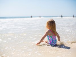 Mädchen im badeanzug sitzt am Strand und spielt in den Wellen