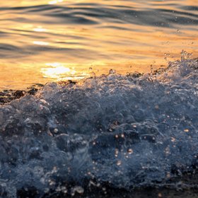 Welle bricht an Strand bei Sonnenuntergang