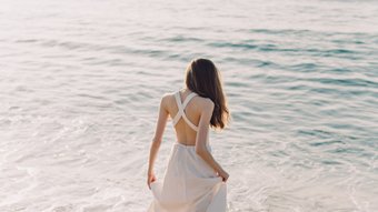 Frau in weißem Kleid läuft am Strand