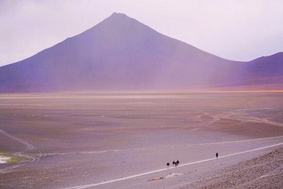 Menschen wandern in karger Landschaft mit Vulkan im Hintergrund