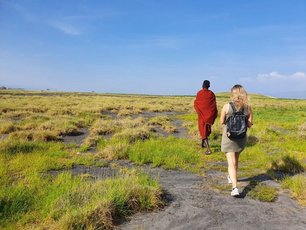 Eine Touristin folgt einem Massai durch die Savanne