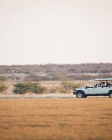 Ein offener Jeep mit Gästen fährt durch die karge Landschaft Botswanas