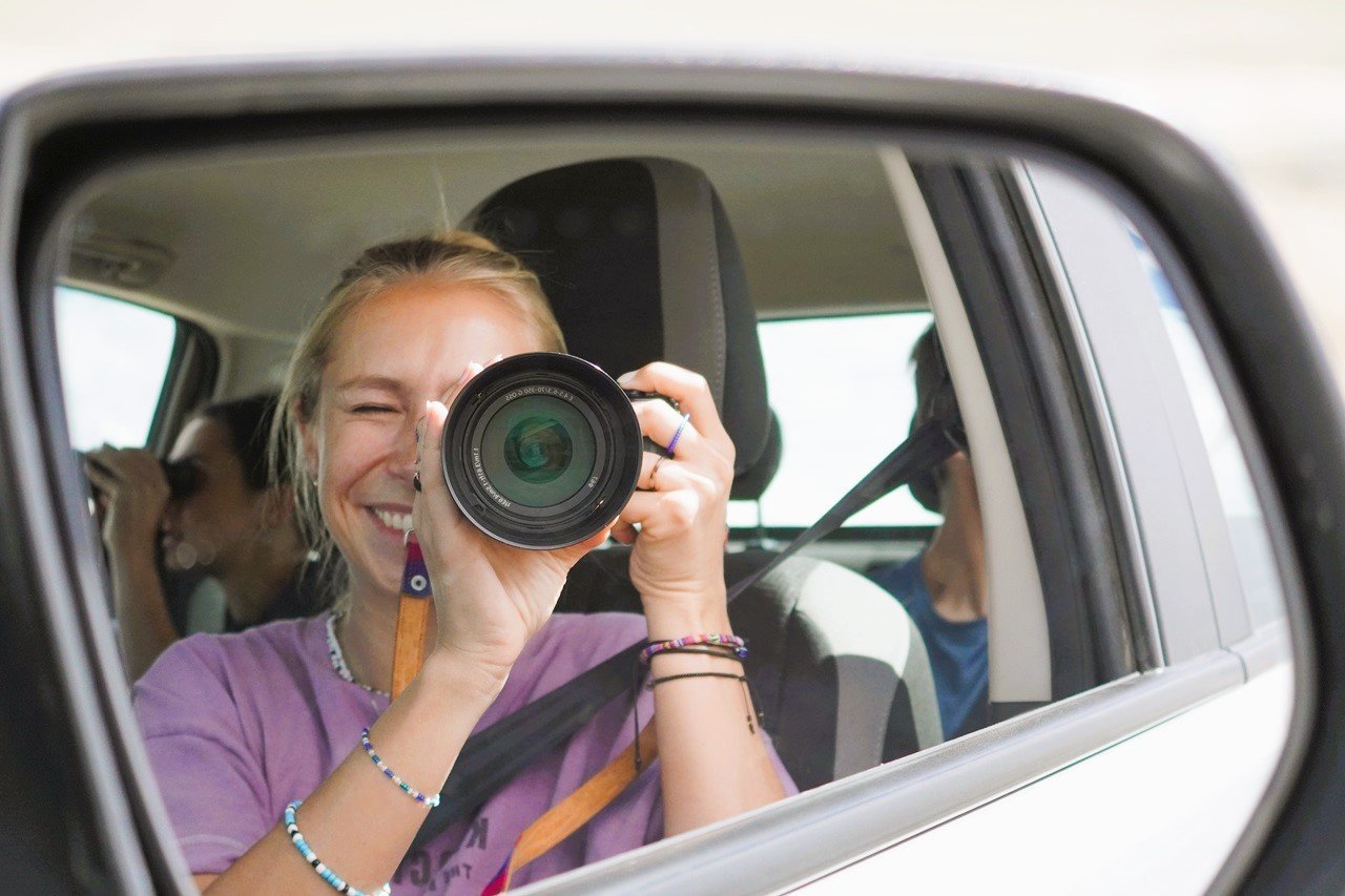 Frau fotografiert sich selbst im Seitenspiegel eines Mietwagens