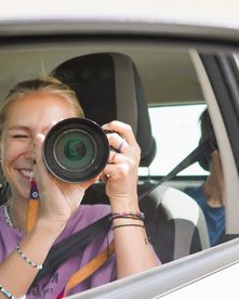 Frau fotografiert sich selbst im Seitenspiegel eines Mietwagens