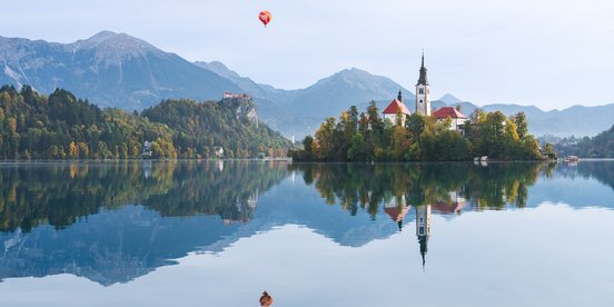 Kirche auf einer kleinen Insel spiegelt sich im See mit Bergen im Hintergrund