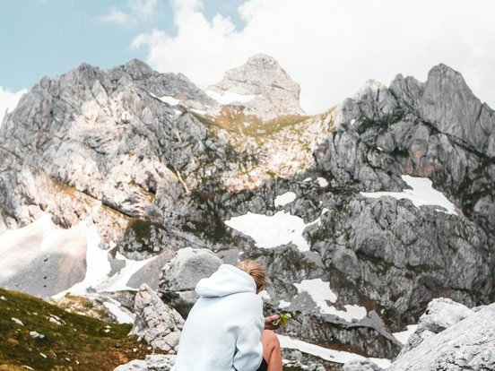 Frau sitzt auf einem Stein in den Bergen und ruht sich vom Wandern aus