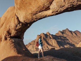 Frau steht unter einer riesigen, natürlichen Felsbrücke
