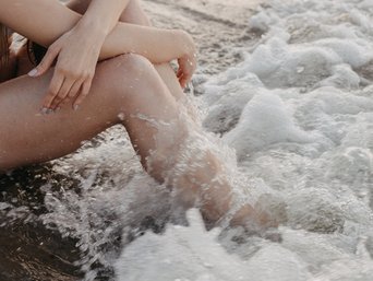 Frau sitzt am Strand und Welle überspült ihre Beine