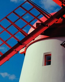 Weiße Windmühle mit knallrotem Rad vor blauem Himmel