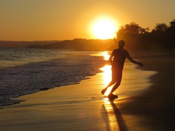 Mensch rennt im Sonnenuntergang am Strand entlang im Gegenlicht