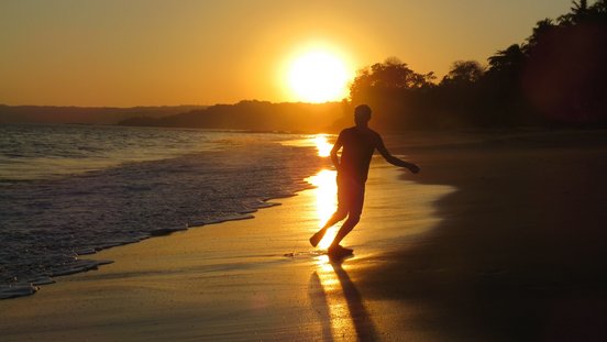 Mensch rennt im Sonnenuntergang am Strand entlang im Gegenlicht